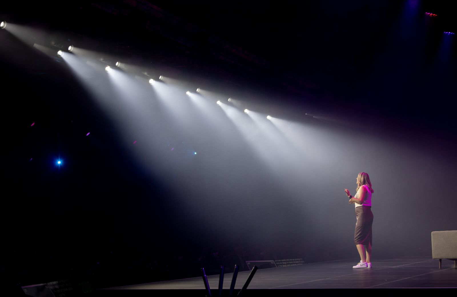 A speaker stands alone on the Money 20/20 Main Stage as a row of theatrical spotlights cut through the haze above her