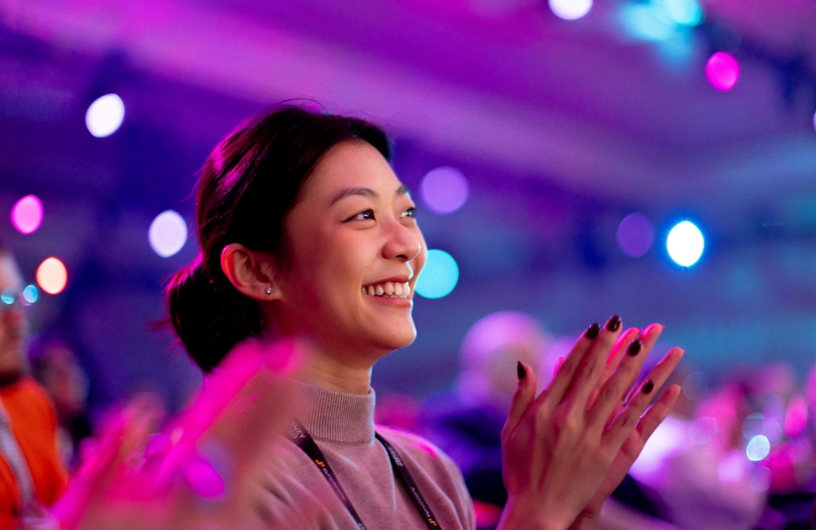 Attendee smiling and clapping in the crowd, lit with magenta and purple stage bokeh